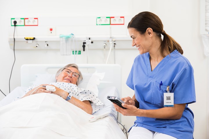 Sitting caregiver holds smart phone device while conversating with a monitored patient in bed
