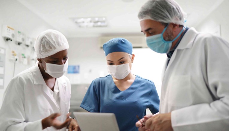 Three doctors in scrubs having a discussion about something they are seeing on a tablet