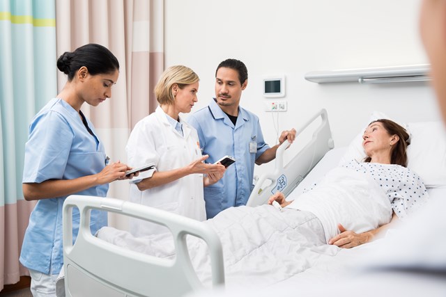 Clinical team with three people around female patient's bed while two of them holding a smartphone device