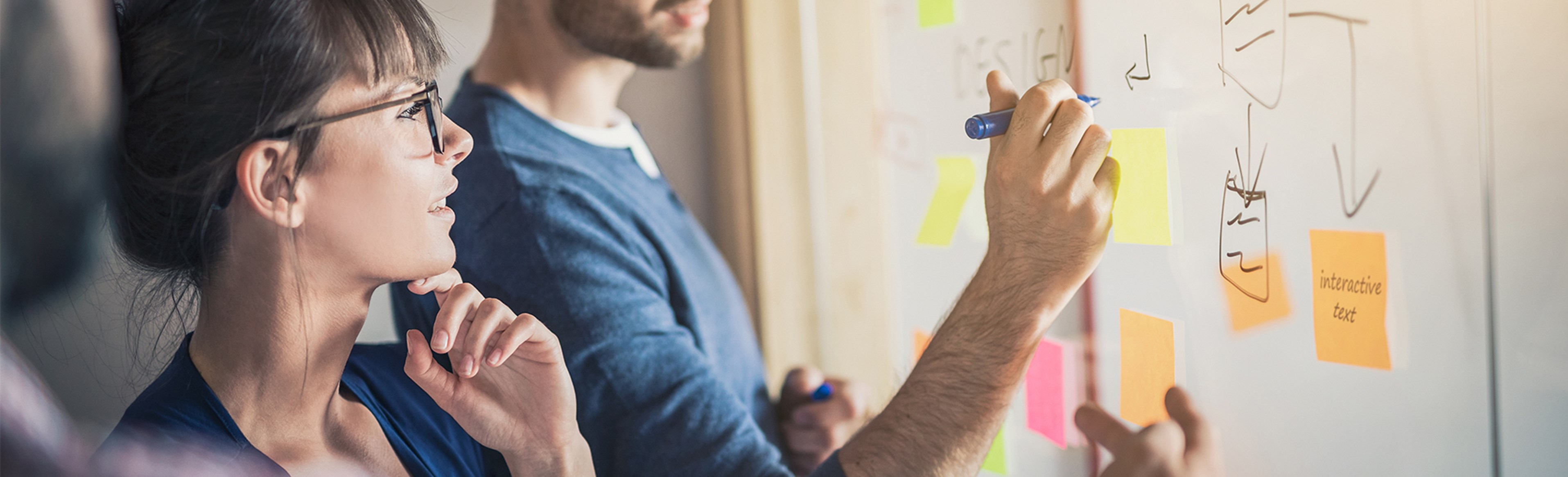 Diversity team in a project design meeting, writing and adding sticky notes on a whiteboard