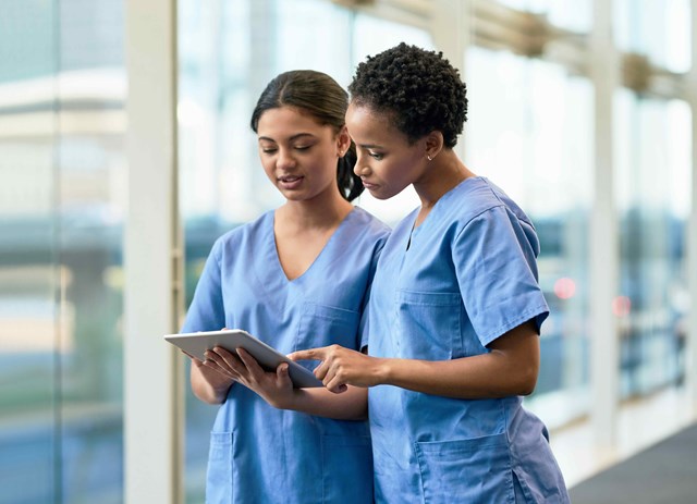 Two nurses in blue scrubs looking at something on a tablet