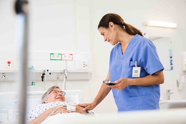 A nurse checking on a patient with a smartphone in her hand