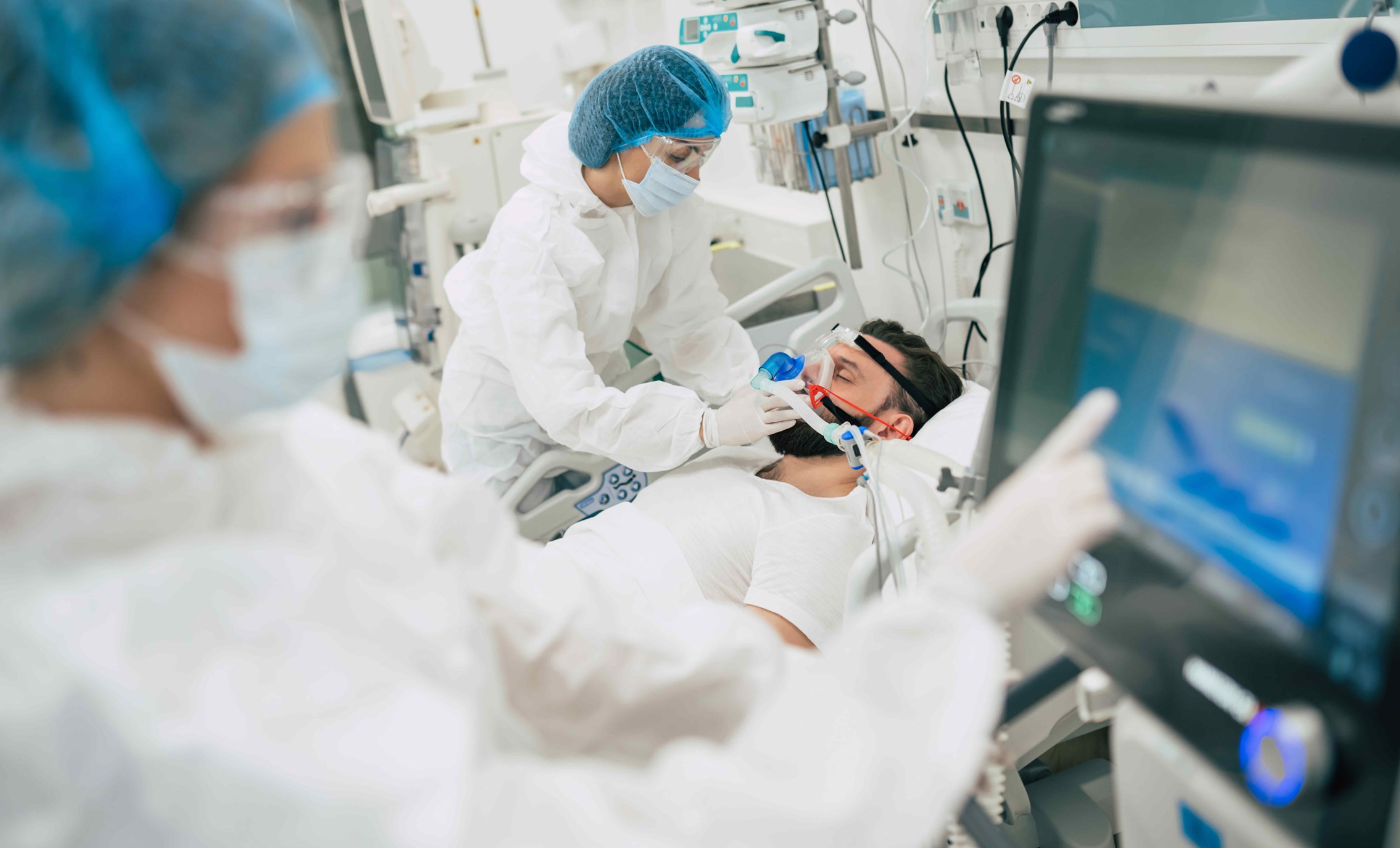 Intubated patient in hospital bed assisted by medical personnel.