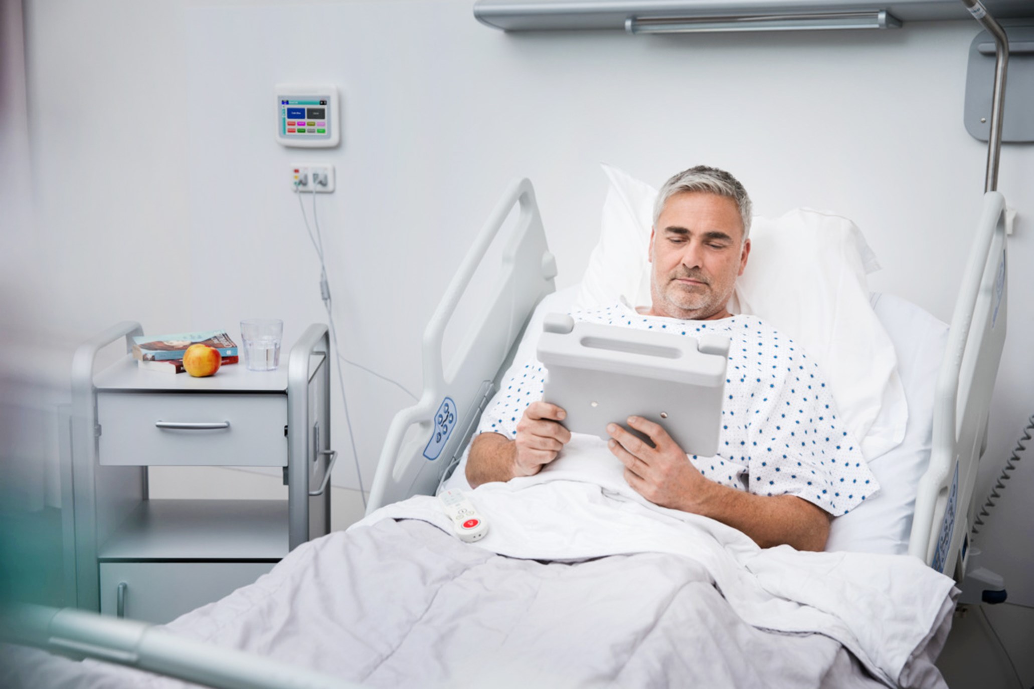 Male patient in bed, holding a tablet.