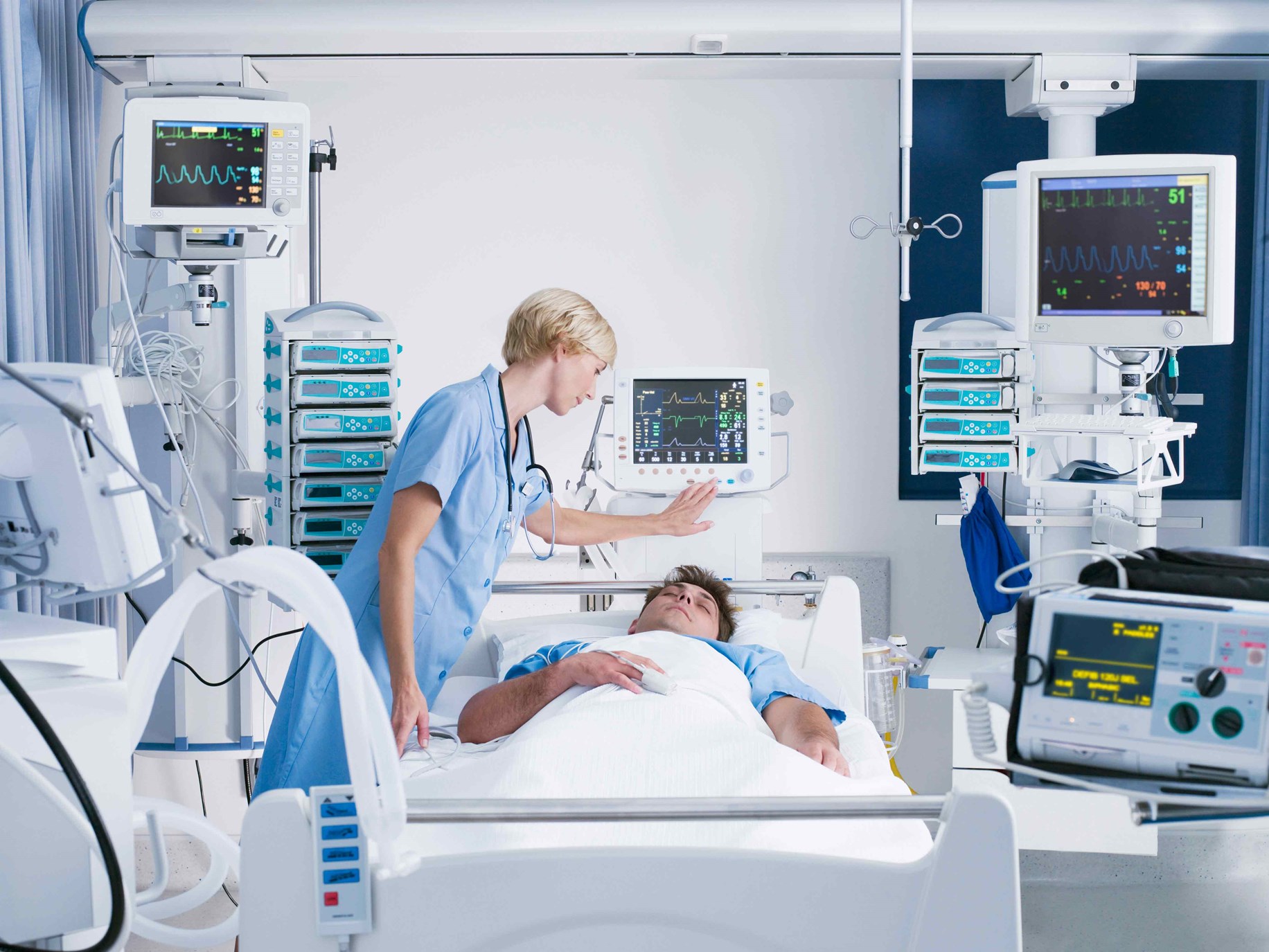 Rounding nurse checks on sleeping patient connected to multiple medical devices.