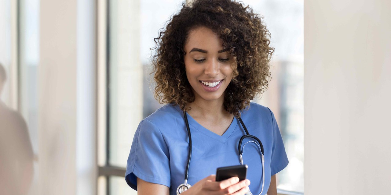 A female nurse in scrubs is looking at her cell phone