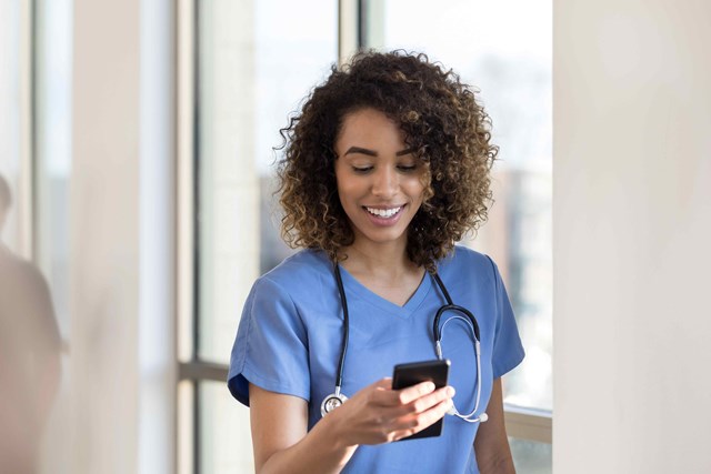 A female nurse in scrubs is looking at her cell phone