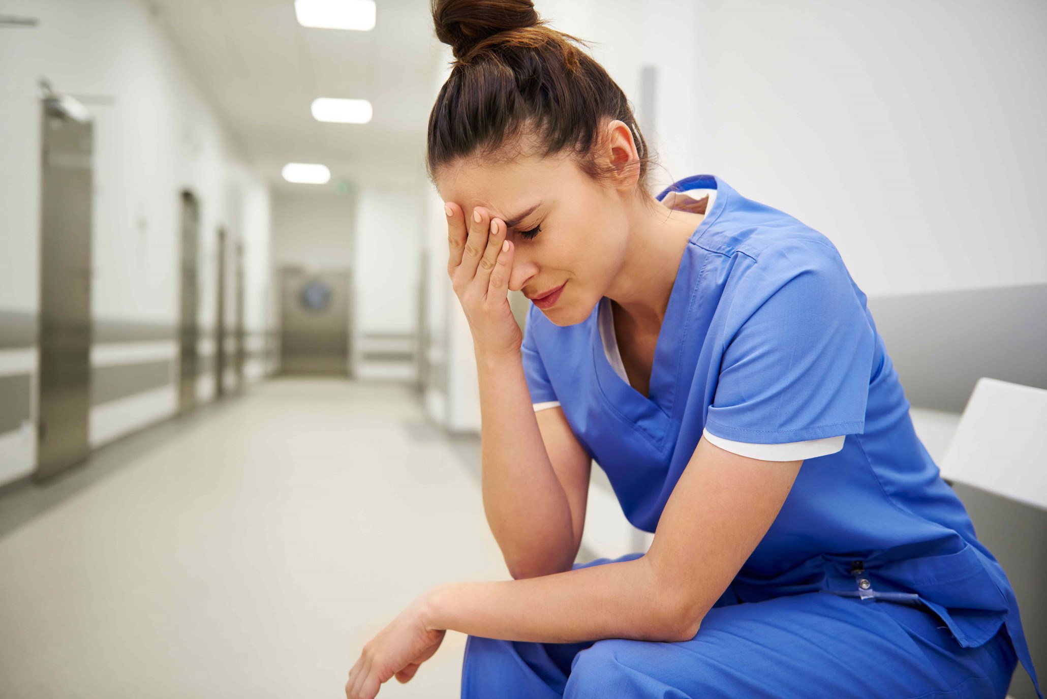 Tired nurse sitting with her head down in hospital hallway