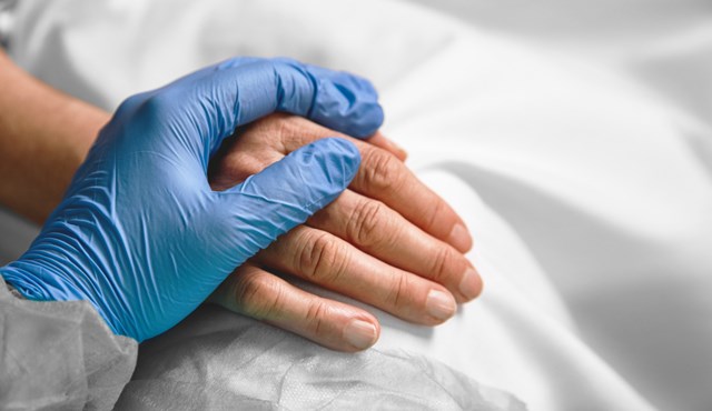 Detail of caregiver's hand in blue surgical gloves holding the hand of a patient