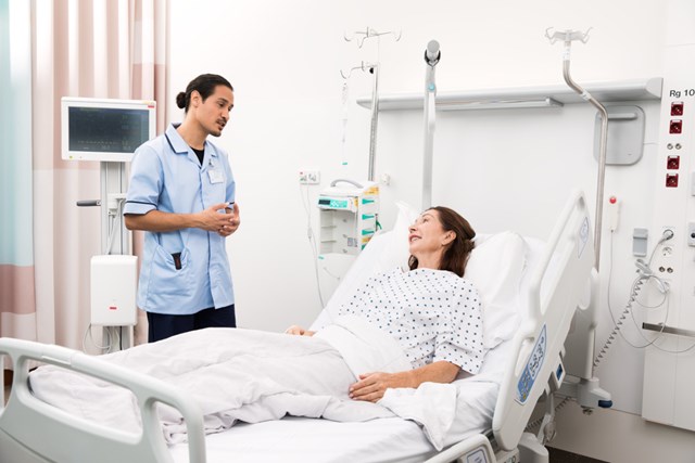 A standing male nurse interacts with a female patient in bed