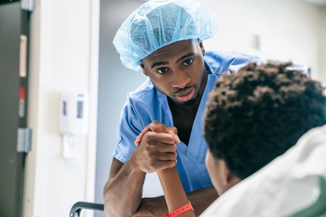 Close-up of a male nurse holding the hand of a patient resting in bed