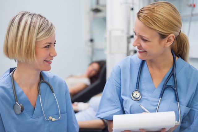 Close-up of two female doctors or nurses wearing blue scrubs and stethoscopes, talking to each other