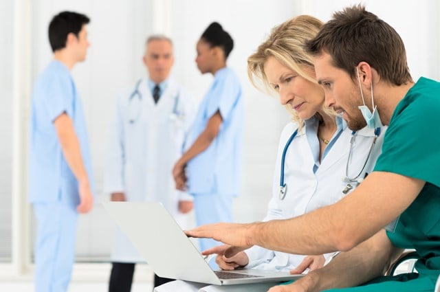 Two doctors discussing in the foreground with three doctors having a discussion in blurred background