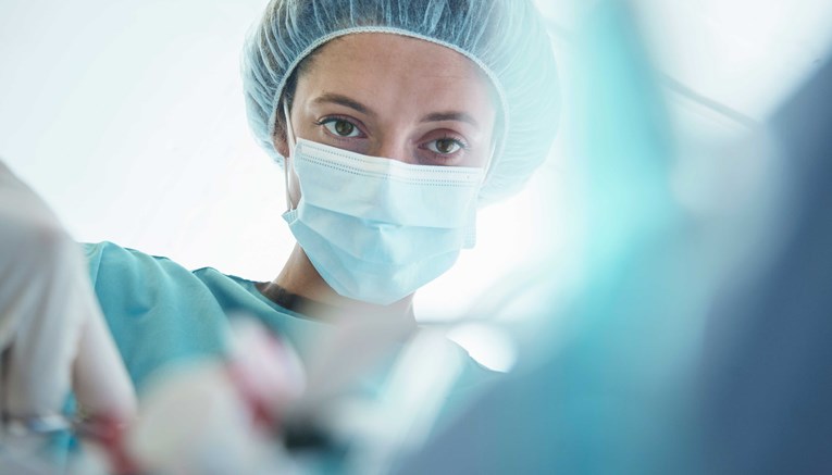 Close-up portrait of a woman doctor wearing a hair net, scrub cap, surgical mask, scrubs, performing a surgery