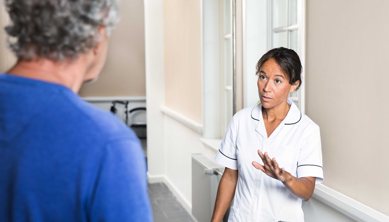 Caregiver in uniform signaling elderly resident to stop going towards her with device in her pocket