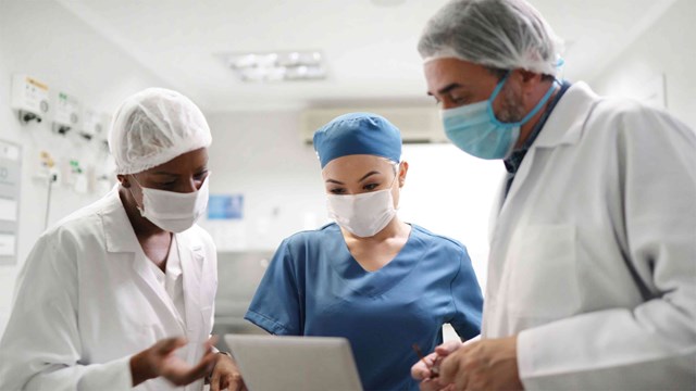 Three doctors in scrubs having a discussion about something they are seeing on a tablet