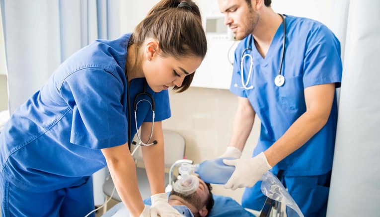 Two nurses in blue scrubs and stethoscopes performing CPR on a patient