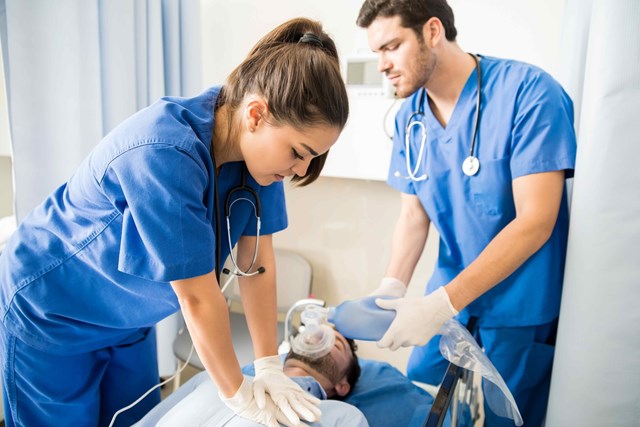 Two nurses in blue scrubs and stethoscopes performing CPR on a patient