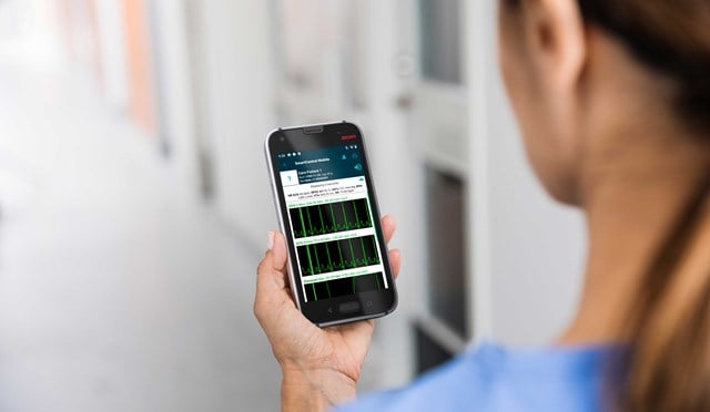 Close-up of a female nurse holding a device in her hand, watching waveforms on the screen