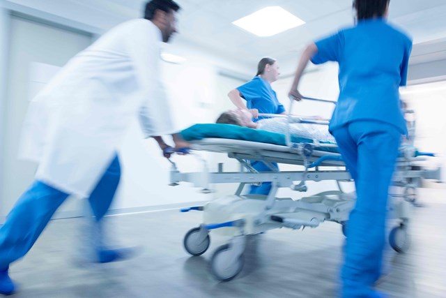 In-motion, blurred image of medical personnel in hospital hallway rushing patient in bed to a hospital room