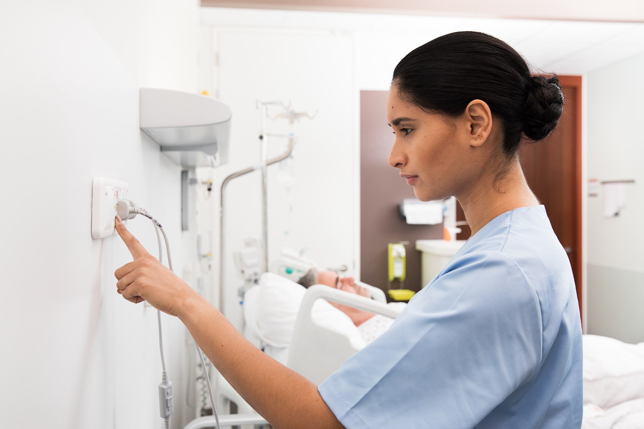 Female nurse or aide pressing telecare Telligence on a wall unit with a male patient.