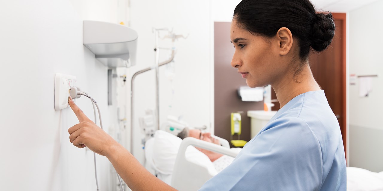 Female nurse or aide pressing telecare Telligence on a wall unit with a male patient.